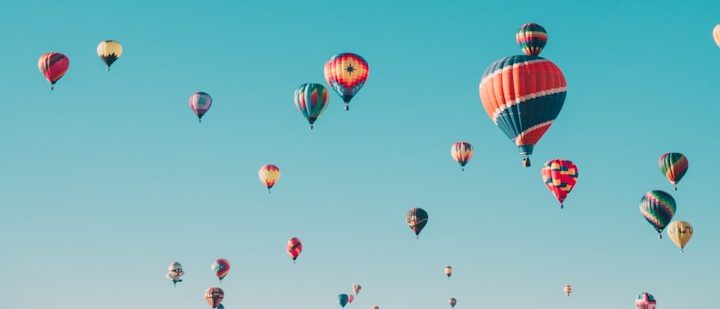 Bunte Heißluftballons steigen vor klarem blauen Himmel auf.