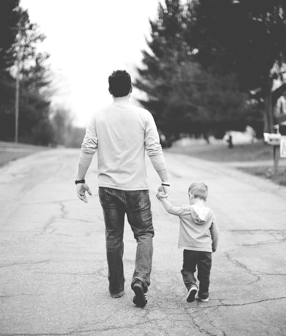 Vater und Kind spazieren Hand in Hand auf einer ruhigen Straße.