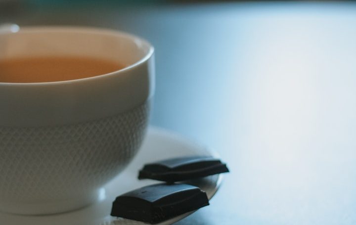 Tasse Tee mit zwei Stückchen dunkler Schokolade auf einem Teller.