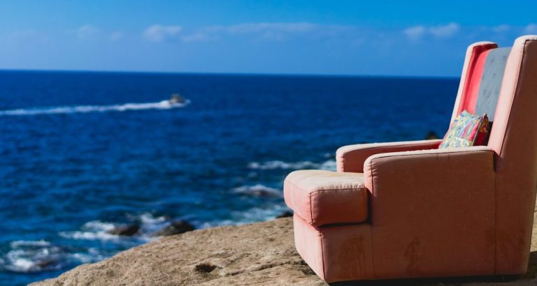 Rosa Couch am Meer mit Blick auf das Wasser und einem Boot in der Ferne.