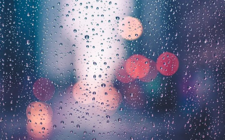 Regentropfen auf einem Fenster mit unscharfen Lichtern im Hintergrund.